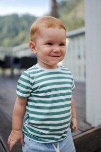 Cute toddler smiling outdoors in green striped shirt on a wooden terrace.
